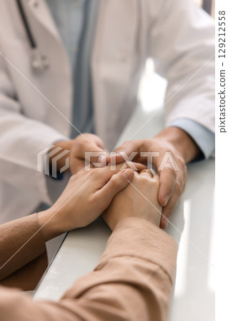 Young doctor man holding hands of female patient Young doctor man holding hands of female patient 129212558