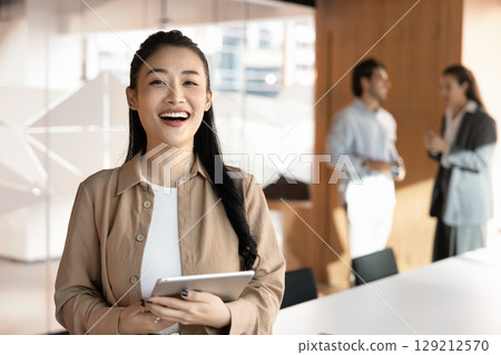 Joyful young woman office worker looking at camera holding tablet 129212570
