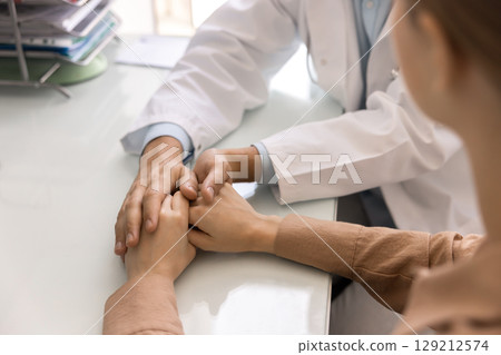 Young doctor man consoling patient, holding hands of woman Young doctor man consoling patient, holding hands of woman 129212574