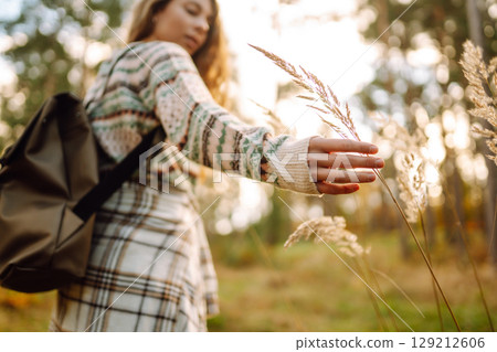 Hand of a stylish tourist with a backpack holds to the soft golden pampas grass in the autumn season 129212606