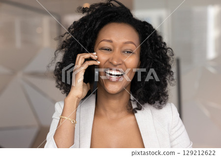 Overjoyed happy millennial Black businesswoman talk on telephone 129212622