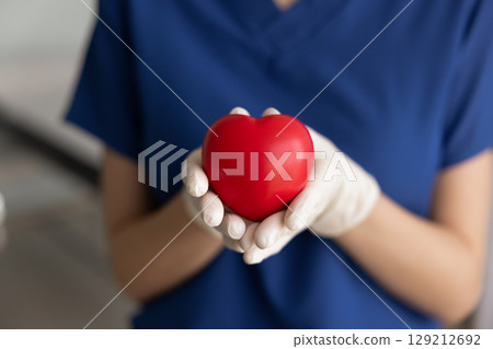 Heart surgeon woman in blue scrubs holding red heart Heart surgeon woman in blue scrubs holding red heart 129212692