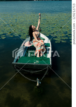 A maiden in a long dress sits in a boat in the middle of the lake 129212713