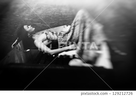 The long dress wraps around the girl's figure as she lies relaxed in a boat on the lake 129212726