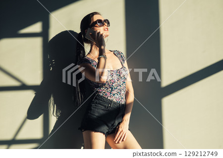 A girl with a long braided ponytail stands against the wall, holding her phone to her ear 129212749
