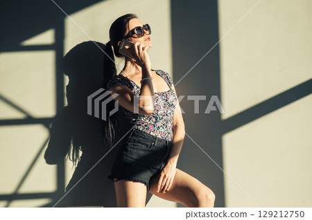 A girl with a long braided ponytail stands against the wall, holding her phone to her ear A girl with a long braided ponytail stands against the wall, holding her phone to her ear 129212750