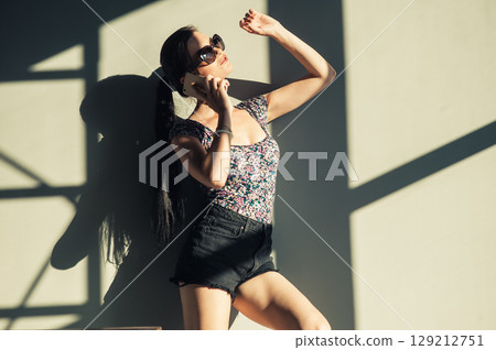 A girl with a long braided ponytail stands against the wall, holding her phone to her ear 129212751