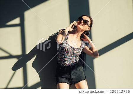 A young woman with a long ponytail stands against the wall, touching the screen of her phone 129212756