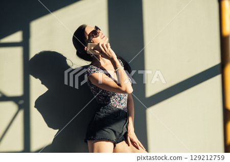 The girl in shorts and a T-shirt is listening attentively to the caller, standing against the wall The girl in shorts and a T-shirt is listening attentively to the caller, standing against the wall 129212759