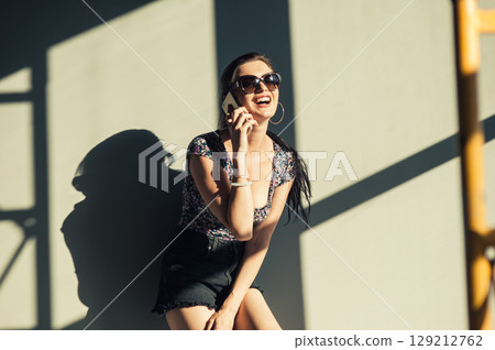 A girl has stopped near the elegant wall with the shadows of the pipes, holding the phone to her ear A girl has stopped near the elegant wall with the shadows of the pipes, holding the phone to her ear 129212762