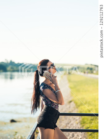A young girl in short shorts and a T-shirt is talking on the phone A young girl in short shorts and a T-shirt is talking on the phone 129212763