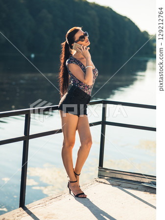 A young girl in short shorts talking on the phone by the lake A young girl in short shorts talking on the phone by the lake 129212764