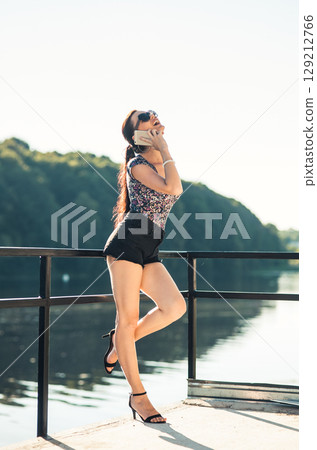 A young girl in short shorts talking on the phone by the lake 129212766