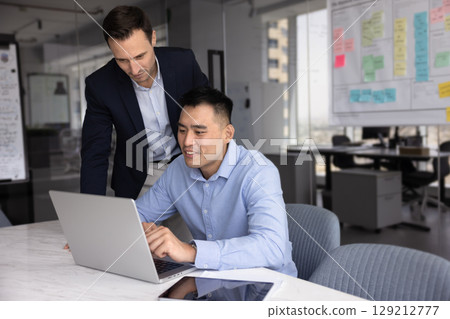 Two multiethnic employees using laptop in modern workplace Two multiethnic employees using laptop in modern workplace 129212777