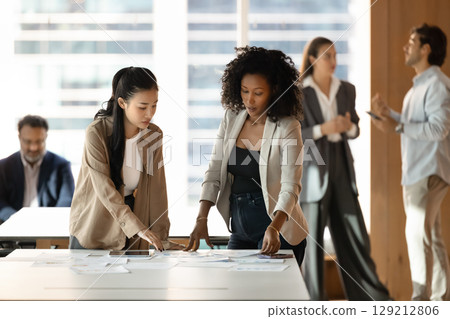 Two young female colleagues review paper documents on office desk 129212806