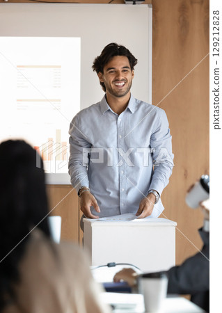 Smiling millennial man business presenter stand at lectern hold speech Smiling millennial man business presenter stand at lectern hold speech 129212828