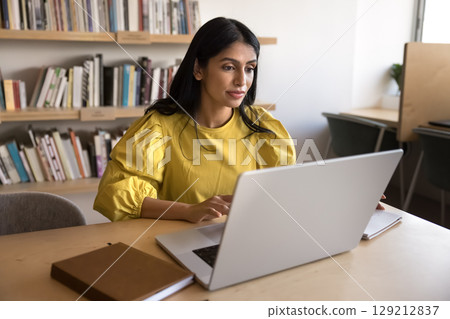 Focused Indian businesswoman working on laptop in workplace Focused Indian businesswoman working on laptop in workplace 129212837