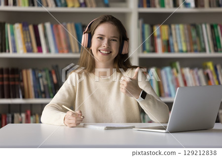 Female student in headphones sitting by notebook showing thumbs up 129212838