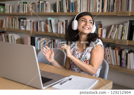 Carefree student woman in headphones listening music seated at table Carefree student woman in headphones listening music seated at table 129212904