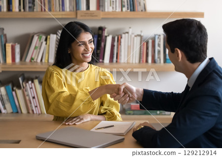 Indian woman and Hispanic man shaking hands across table Indian woman and Hispanic man shaking hands across table 129212914