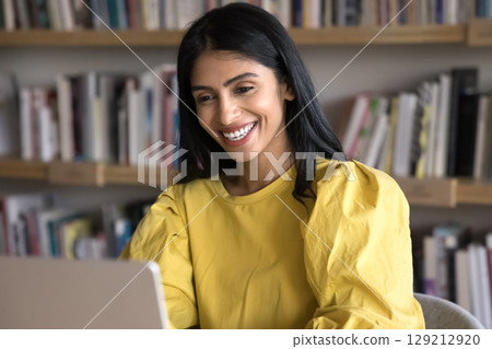 Cheery Indian woman reading pleasant news on laptop and laughing 129212920
