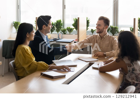 Businessmen shaking hands during formal meeting with teammates in office 129212941