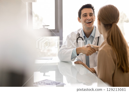 Joyful young Latin physician man shaking hands with female patient Joyful young Latin physician man shaking hands with female patient 129213081