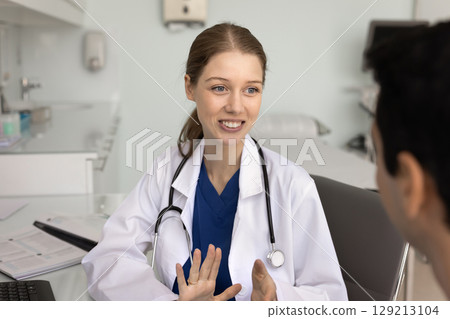 Happy young female GP doctor talking to male patient 129213104