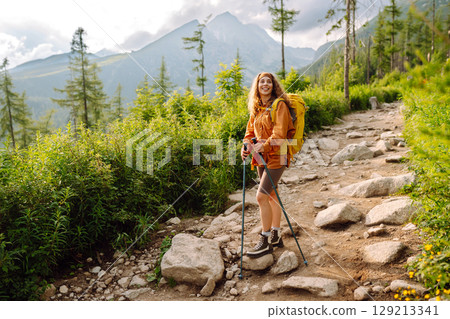 Young woman traveler hiking poles on trail among the mountains. Hiking. Active lifestyle. 129213341