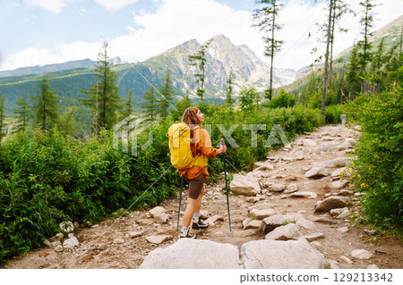 Young woman traveler hiking poles on trail among the mountains. Hiking. Active lifestyle. 129213342