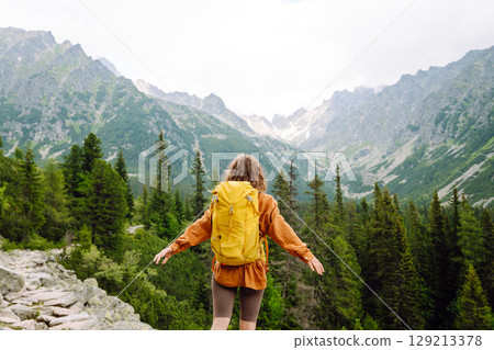 Smiling traveler with a bright backpack on a hiking mountain trail. Active lifestyle. 129213378