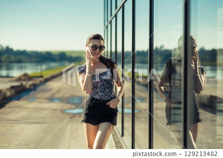 The young lady is enjoying the warm sun without being distracted from the conversation 129213482