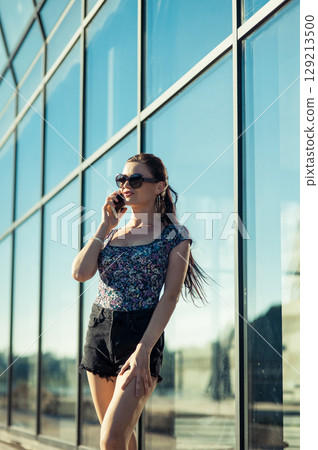 The girl's long braided hair is lying beautifully on her back as she stands by the glass. The girl's long braided hair is lying beautifully on her back as she stands by the glass. 129213500