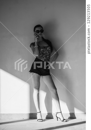 A charming girl is talking on the phone, leaning on the wall. 129213505