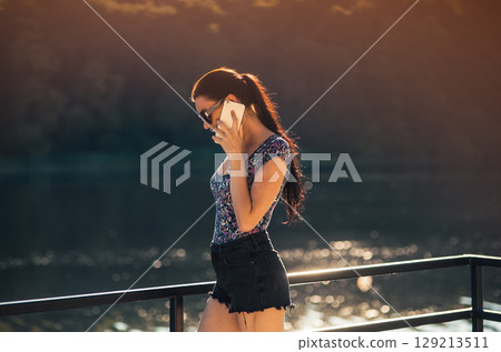 The girl in stylish sunglasses with a braided ponytail stands by the lake The girl in stylish sunglasses with a braided ponytail stands by the lake 129213511
