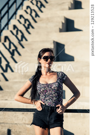 A young girl in shorts is standing near a large staircase, enjoying the sun's warmth A young girl in shorts is standing near a large staircase, enjoying the sun's warmth 129213528