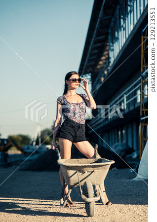A girl with luxurious braided hair stops near scaffolding where bricks and sand lie scattered 129213551