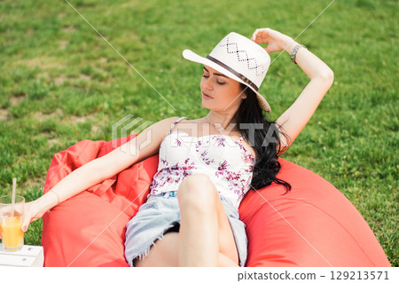 A girl in a light outfit and a hat is sitting in a soft bag against the background 129213571