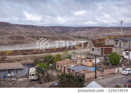 Aerial view of Colonia Libertad, Tijuana, featuring modest homes near the U.S. border fence, with arid hills and overcast skies, reflecting poverty, crime, and immigration challenges. 129214034