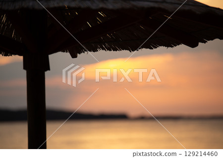Sky with light clouds over the sea. In the foreground a bamboo sunshade. Sunset Sky with light clouds over the sea. In the foreground a bamboo sunshade. Sunset 129214460