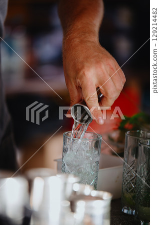 Bartender pours strong alcohol from measuring cup into a glass. Making a Mojito Bartender pours strong alcohol from measuring cup into a glass. Making a Mojito 129214482