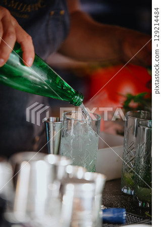 Bartender pouring sparkling water into a glass. Making a Mojito cocktail 129214484