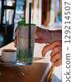 A customer at a beach bar picks up an ice-cold Mojito cocktail with paper straw 129214507