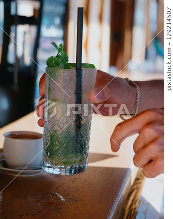 A customer at a beach bar picks up an ice-cold Mojito cocktail with paper straw A customer at a beach bar picks up an ice-cold Mojito cocktail with paper straw 129214507