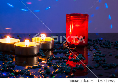 A diamond-studded gold ring is placed among burning candles that softly light the scene A diamond-studded gold ring is placed among burning candles that softly light the scene 129214600