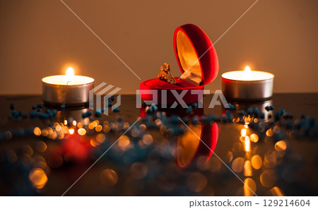 A golden ring lies next to candles burning in the dark 129214604