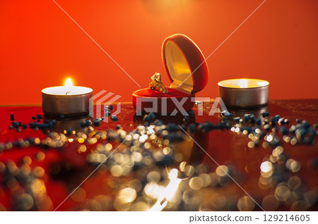 A golden ring lies next to candles burning in the dark 129214605