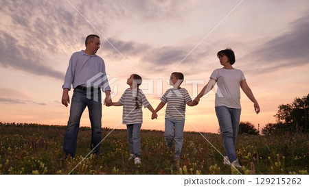 mother father children boy girl park sunset, man woman toddlers outdoors, Happy family walking in a field at sunset, Parents and children holding hands together, Family enjoying nature outdoors 129215262