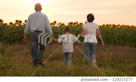Family mother father man woman parent walking through field with child sunflowers at sunset, Happy family time girl child outdoors, Parents holding hands with child, Sunset walk in countryside in Family mother father man woman parent walking through field with child sunflowers at sunset, Happy family time girl child outdoors, Parents holding hands with child, Sunset walk in countryside in 129215277