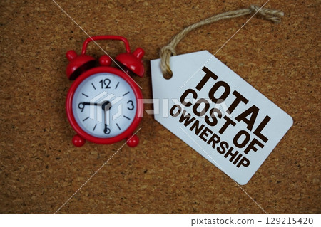 TCO abbreviation of Total Cost of Ownership text on price tag with alarm clock on cork board background 129215420